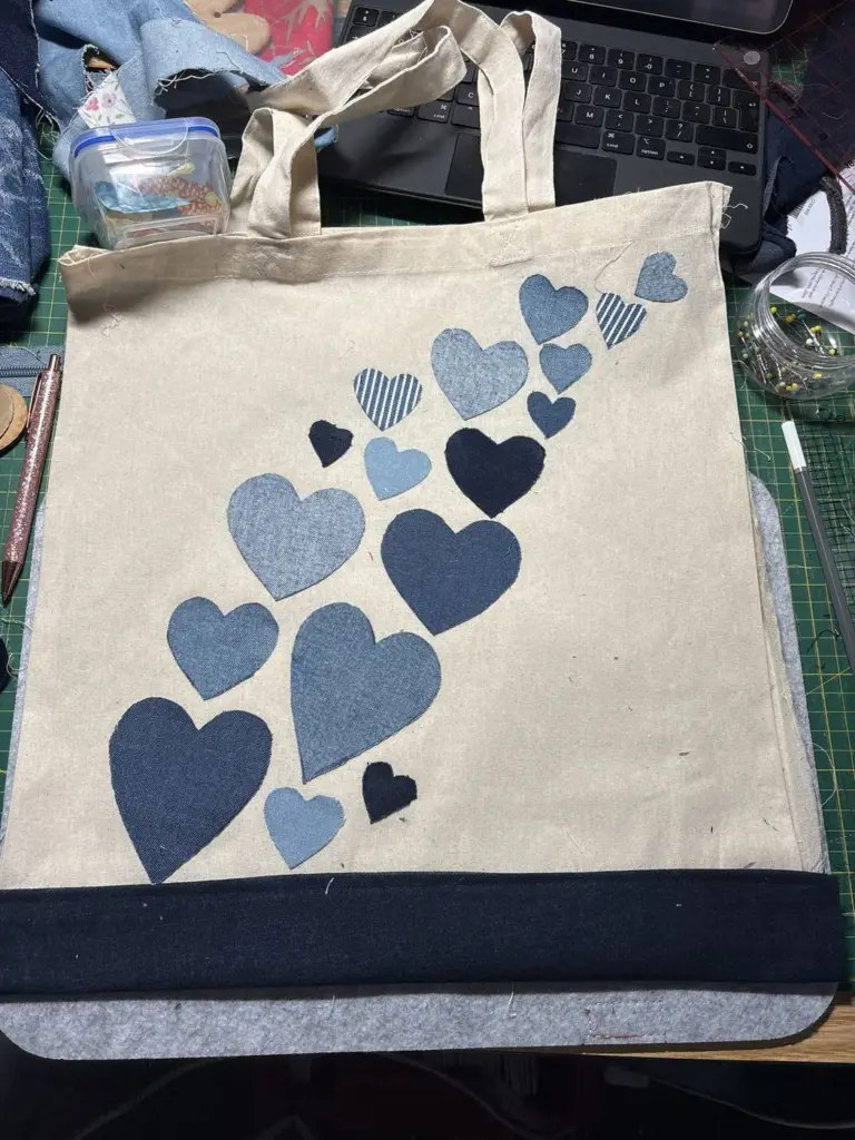 A canvas tote bag with a trail of appliqué denim hearts