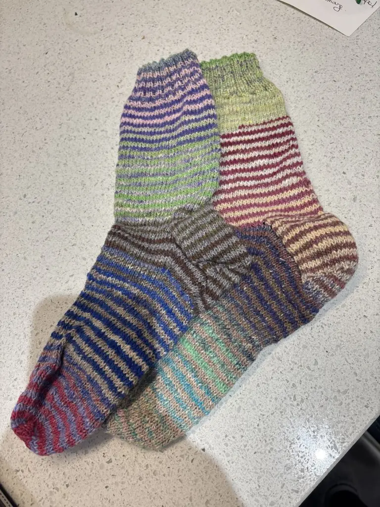 A pair of hand knitted striped socks in purple, green and grey